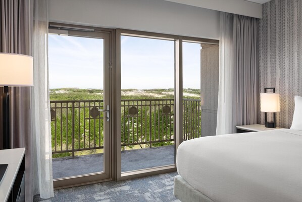 Hotelkamer met een groot bed, een bureau, een stoel, een balkon met uitzicht op groen en een raam met gordijnen.