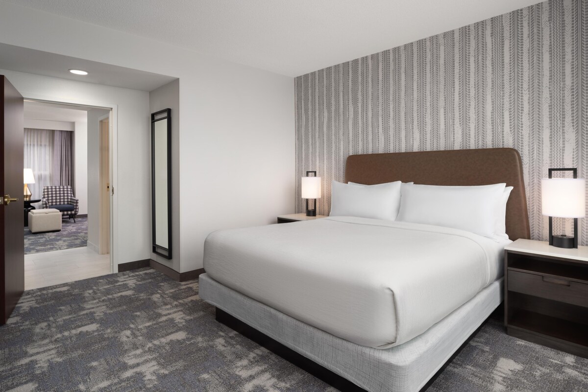 Une chambre d’hôtel avec un grand lit, deux tables de chevet avec des lampes, un grand miroir et une moquette à motifs.