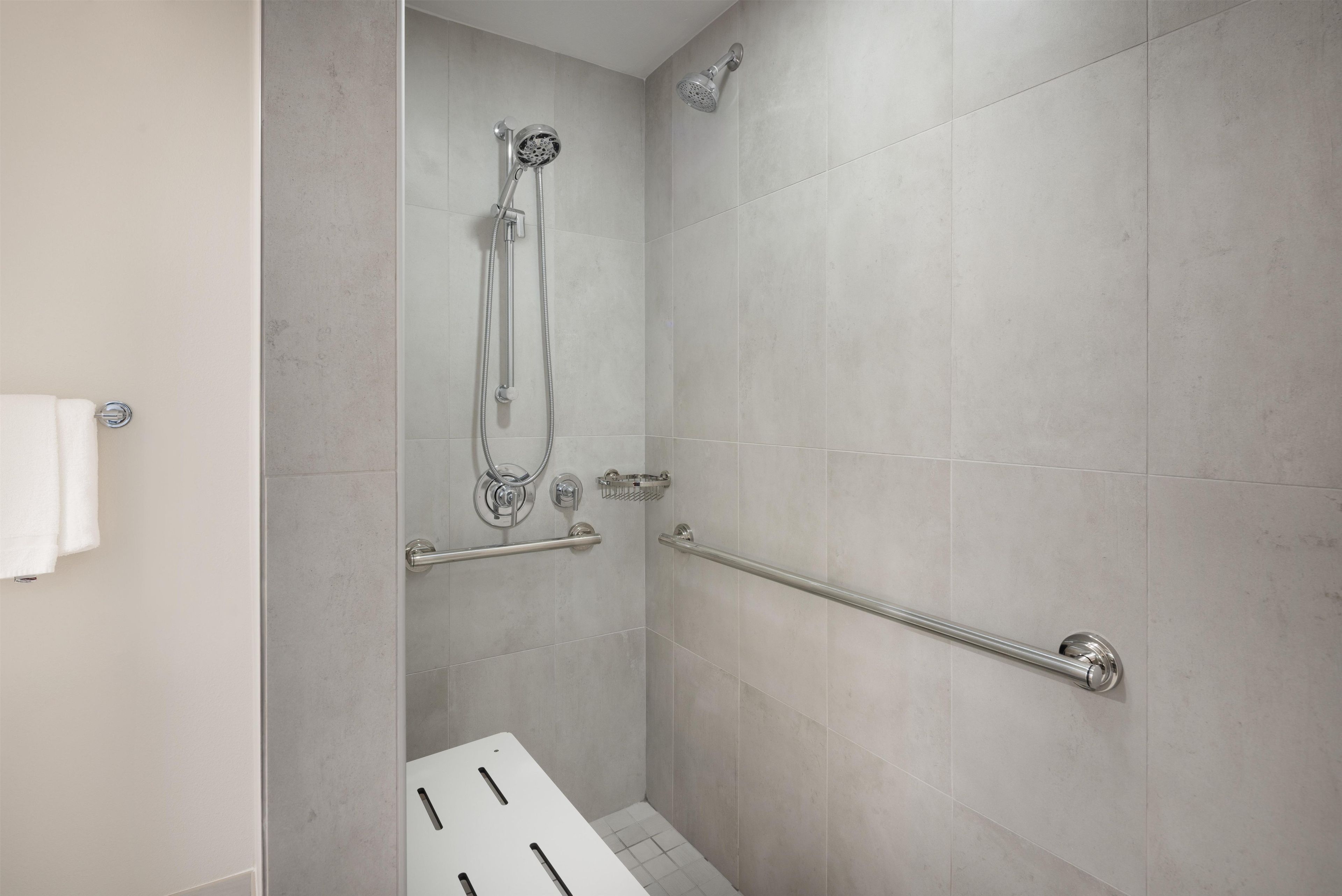 A modern bathroom with a walk-in shower, grab bars, and a towel rack.