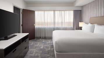 A hotel room with a bed, a TV on a dresser, a window with curtains, and a lamp.