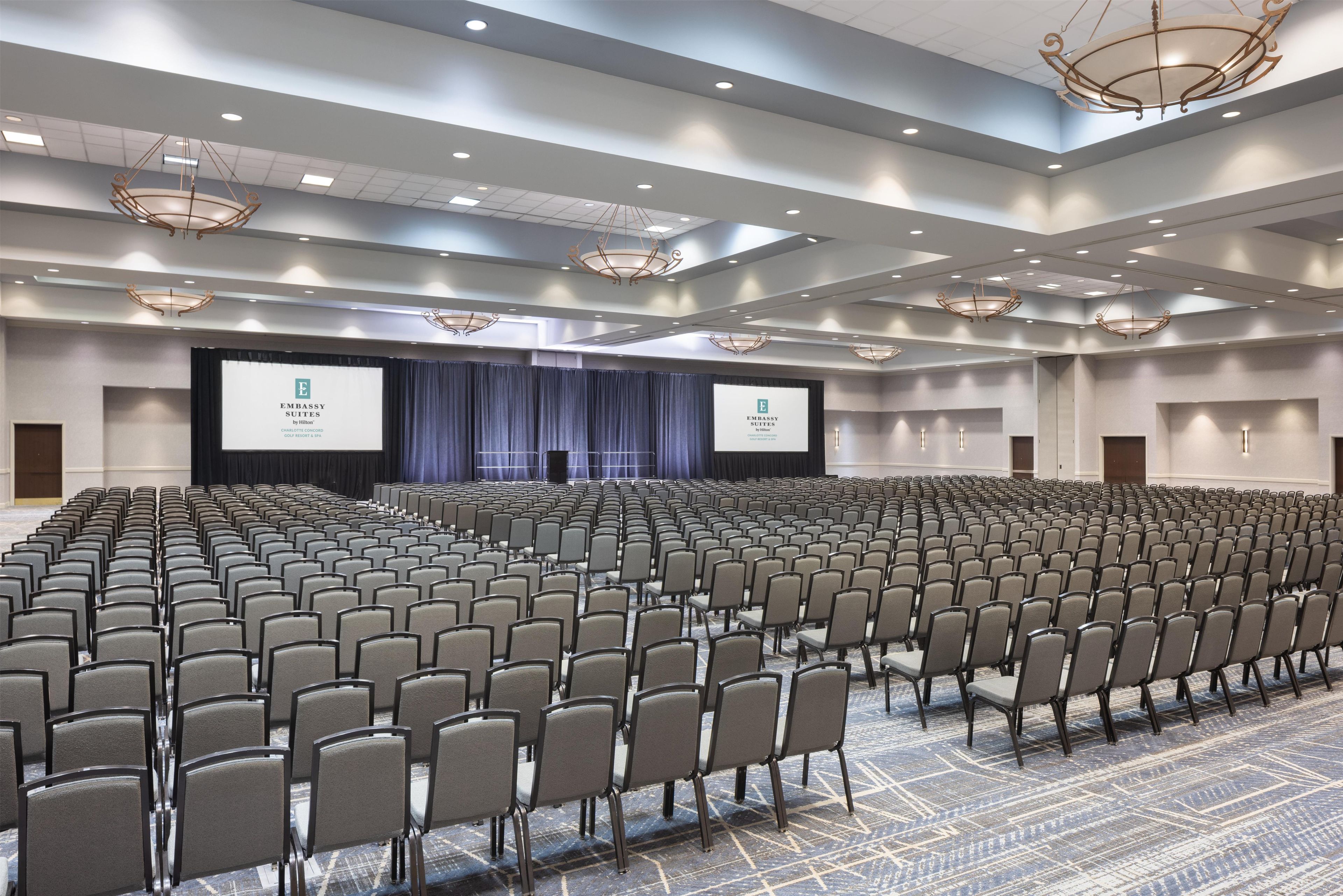 A large conference room with rows of chairs, a stage with a screen, and a chandelier.