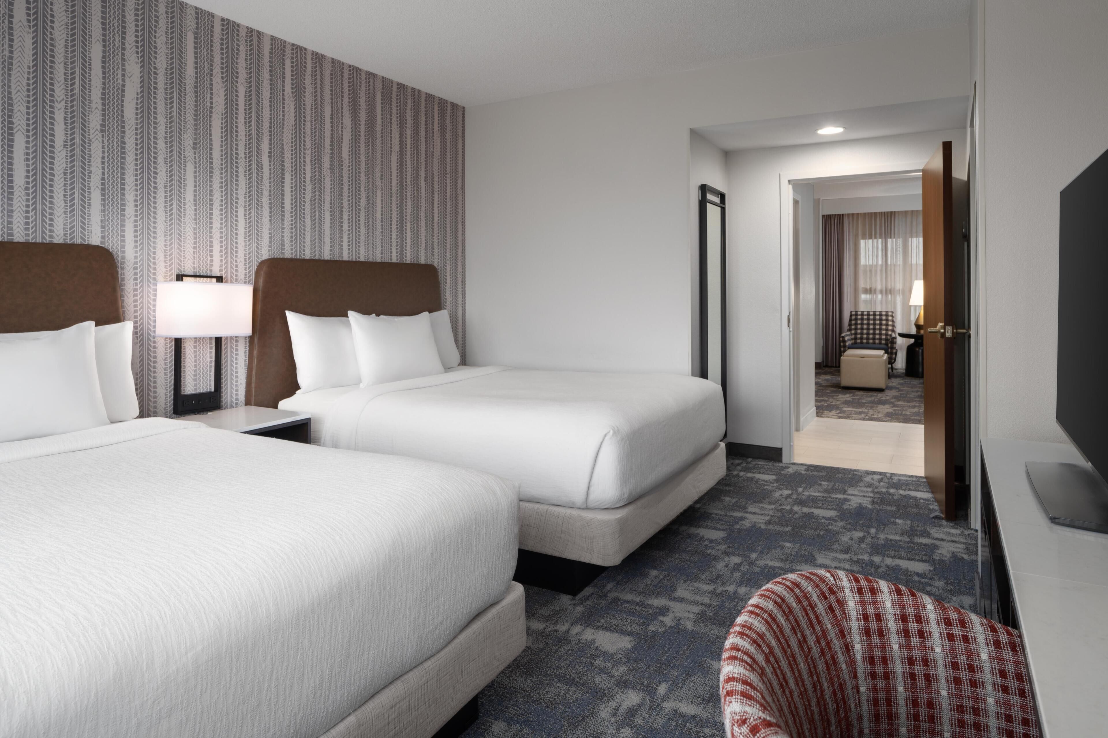 Une chambre d’hôtel avec deux lits, un bureau, une chaise, une télévision et un mur décoré d’un motif.