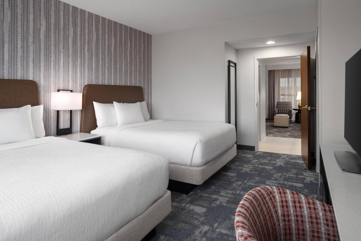 Une chambre d’hôtel avec deux lits, un bureau, une chaise, une télévision et un mur décoré d’un motif.