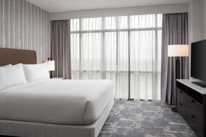 Une chambre d’hôtel avec un grand lit, une télévision, un bureau et une vue sur l’extérieur à travers des rideaux transparents.
