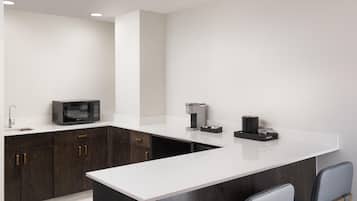 Una cocina moderna con armarios de madera oscura, encimera blanca, microondas, cafetera y dos sillas.