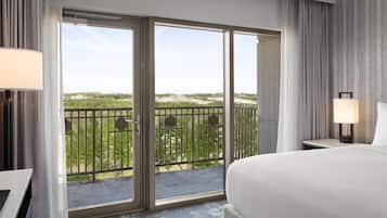 Habitación de hotel con una cama grande, un escritorio, una silla, un balcón con vistas a la vegetación y una ventana con cortinas.