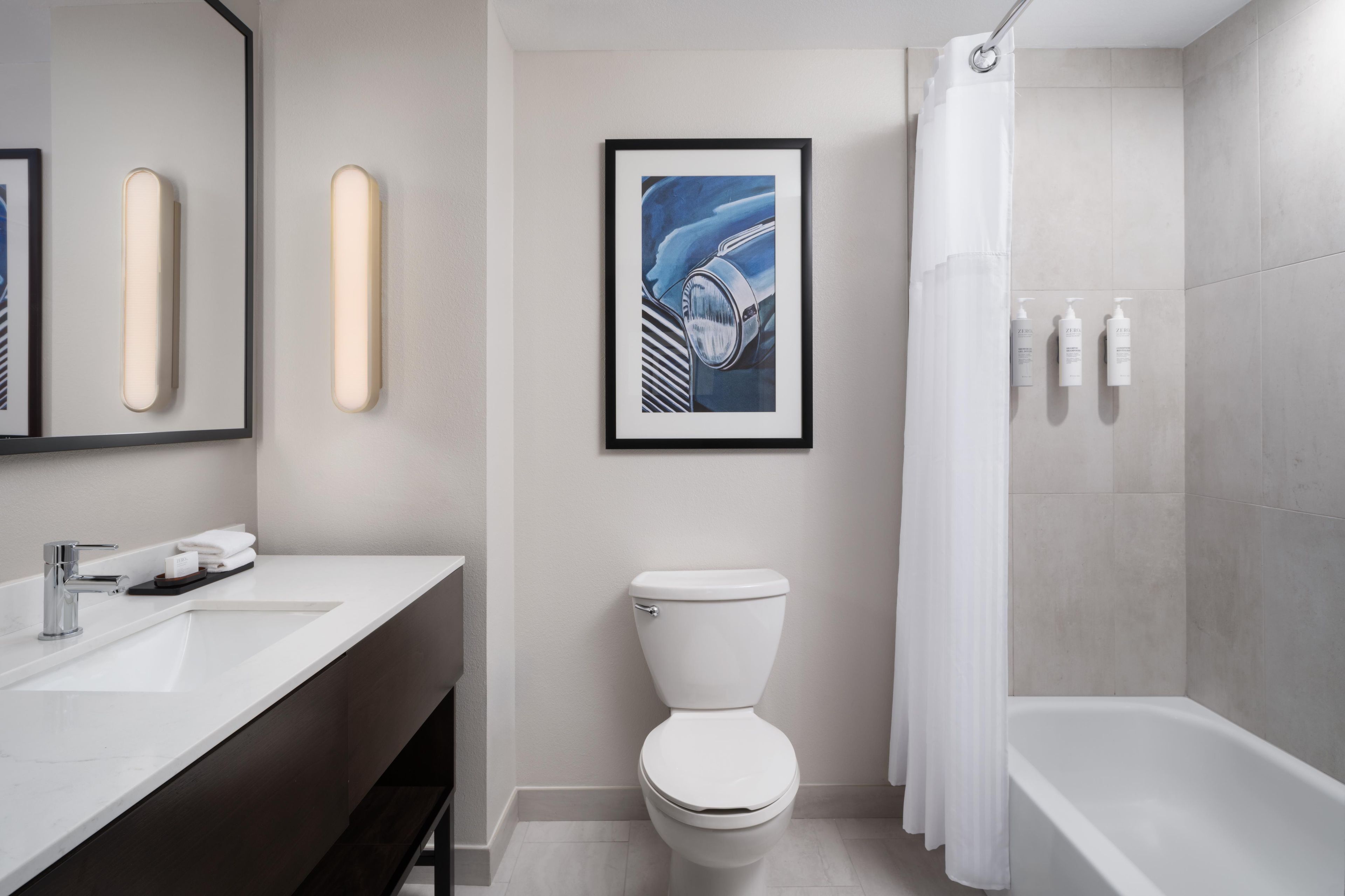 A modern bathroom with a white sink, a framed artwork, a toilet, and a bathtub.