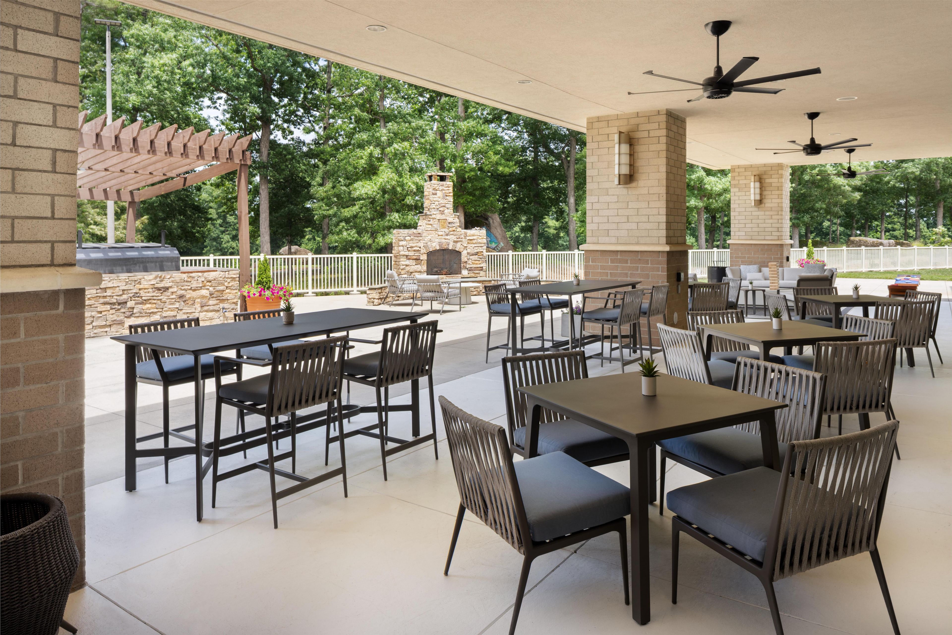 An outdoor patio area with multiple tables and chairs, a stone fireplace, and a pergola.