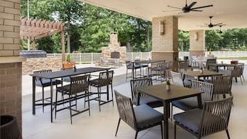 An outdoor patio area with multiple tables and chairs, a stone fireplace, and a pergola.