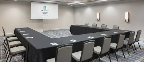 A conference room with a long table, chairs, a projector screen, and a carpeted floor.