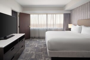 Una habitación de hotel con una cama, un televisor en una cómoda, una ventana con cortinas y una lámpara.