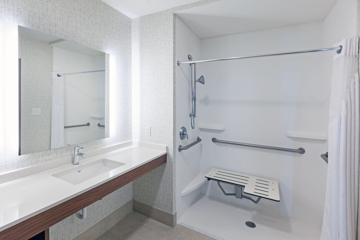 A modern bathroom with two sinks, a shower with grab bars, and a mirror.