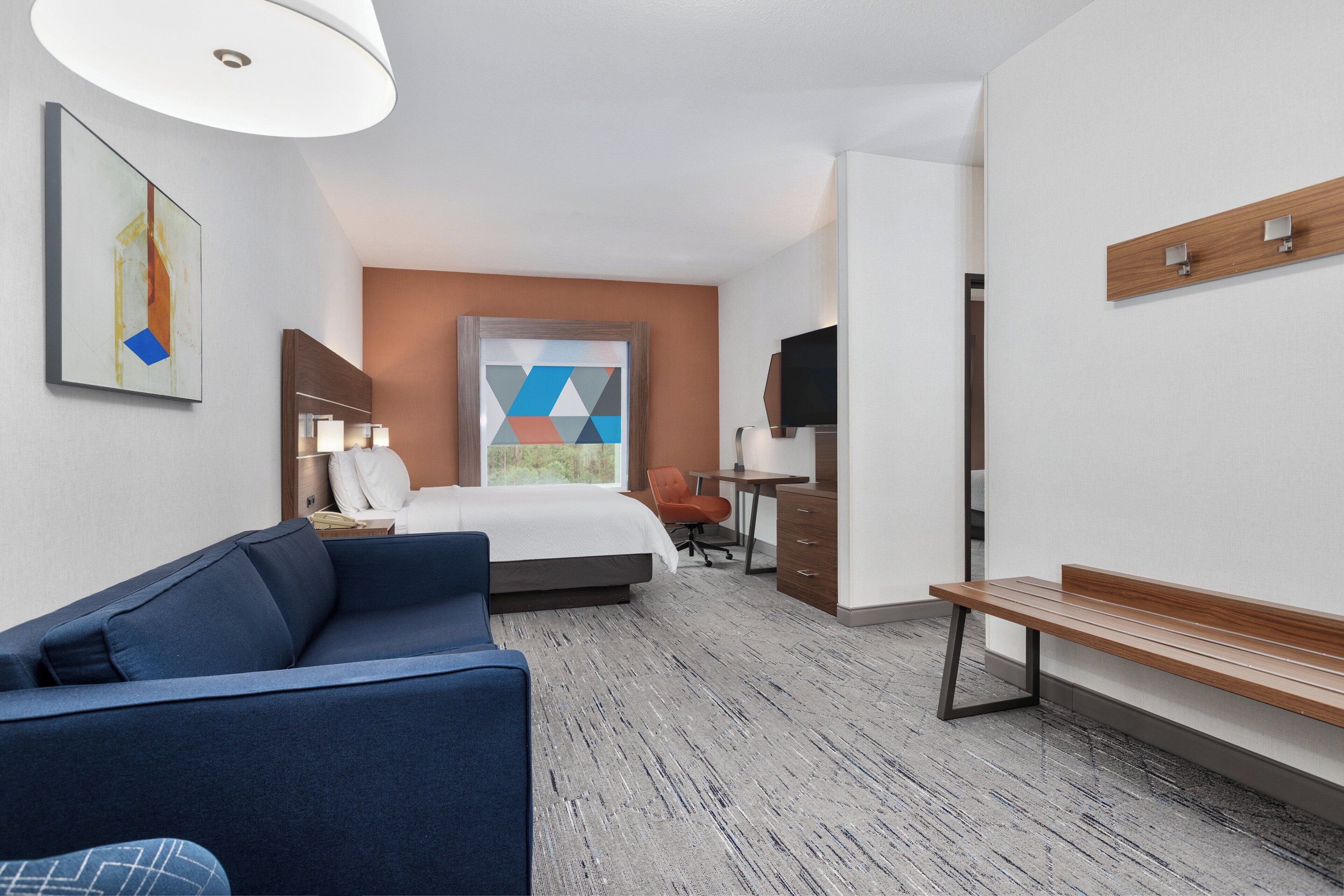 A hotel room with a bed, a desk, a chair, a sofa, and a TV.