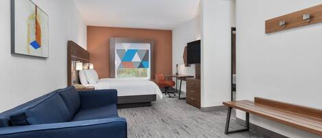 A hotel room with a bed, a desk, a chair, a sofa, and a TV.
