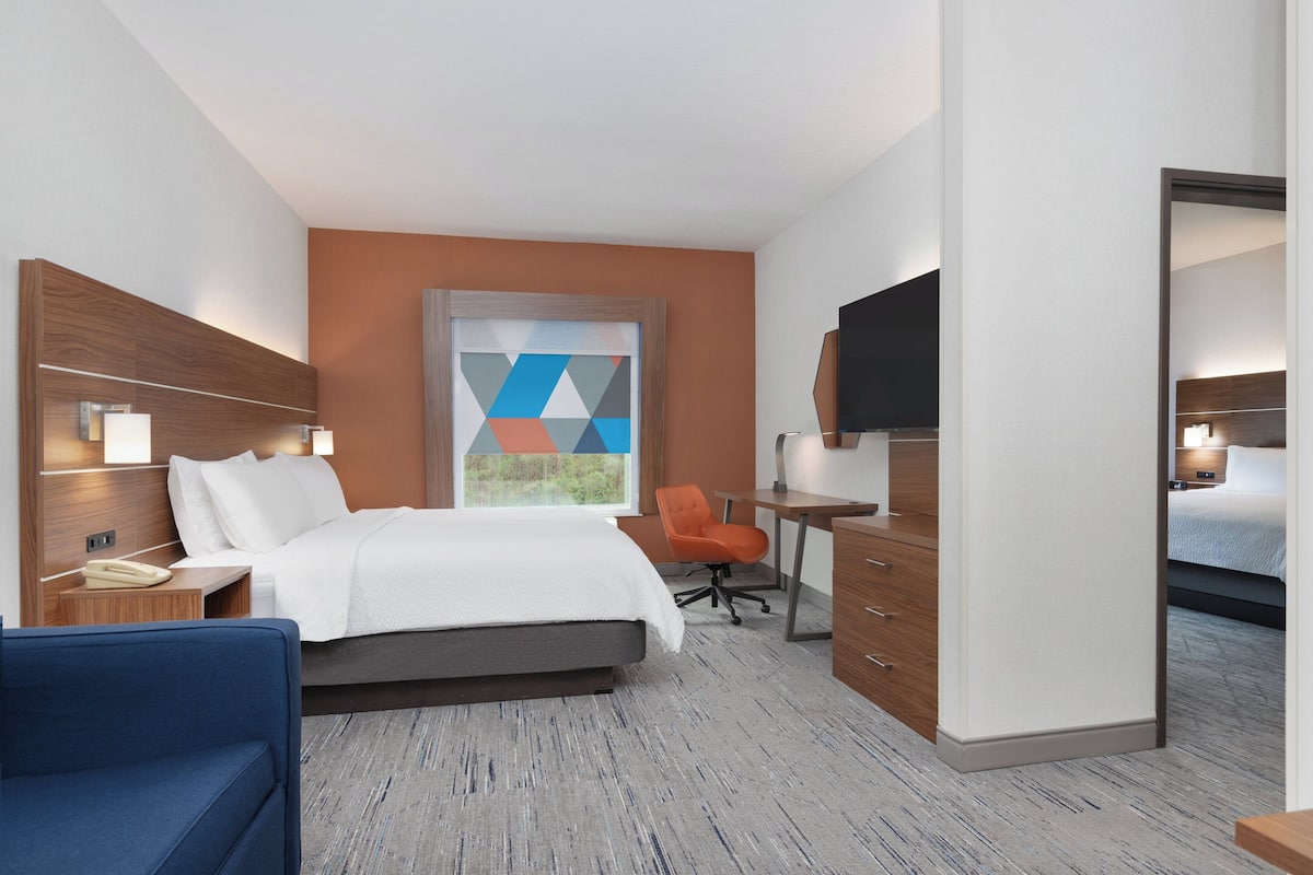 A hotel room with a bed, desk, chair, and TV.