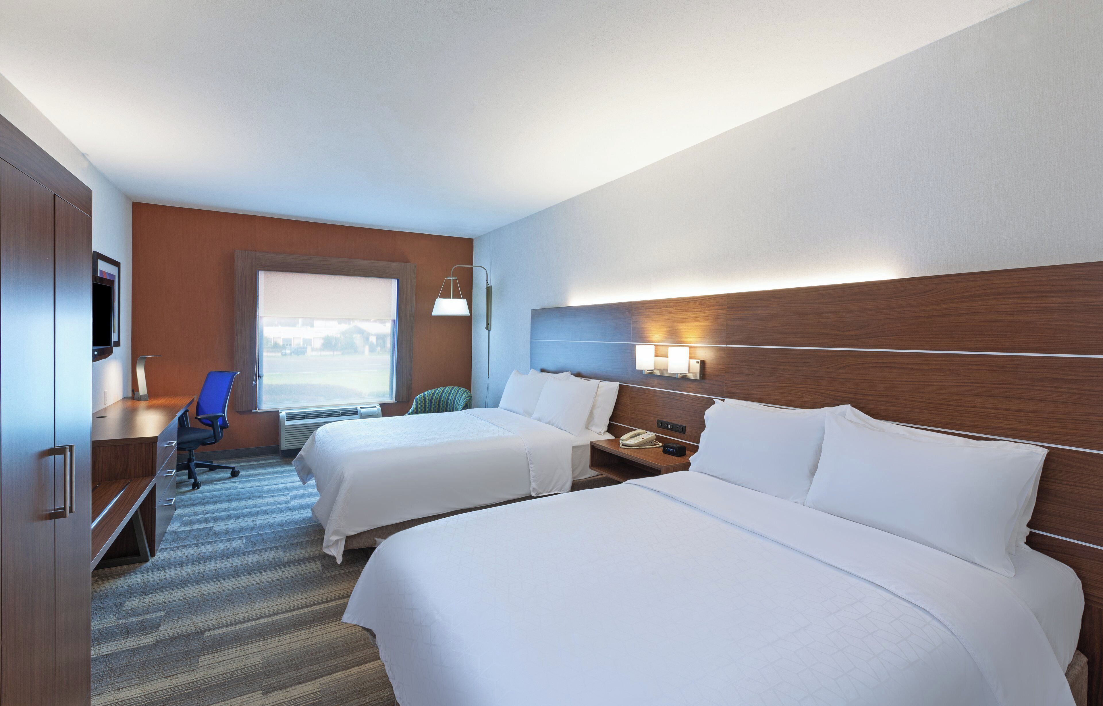 Habitación de hotel con dos camas, un escritorio, una silla y un televisor.