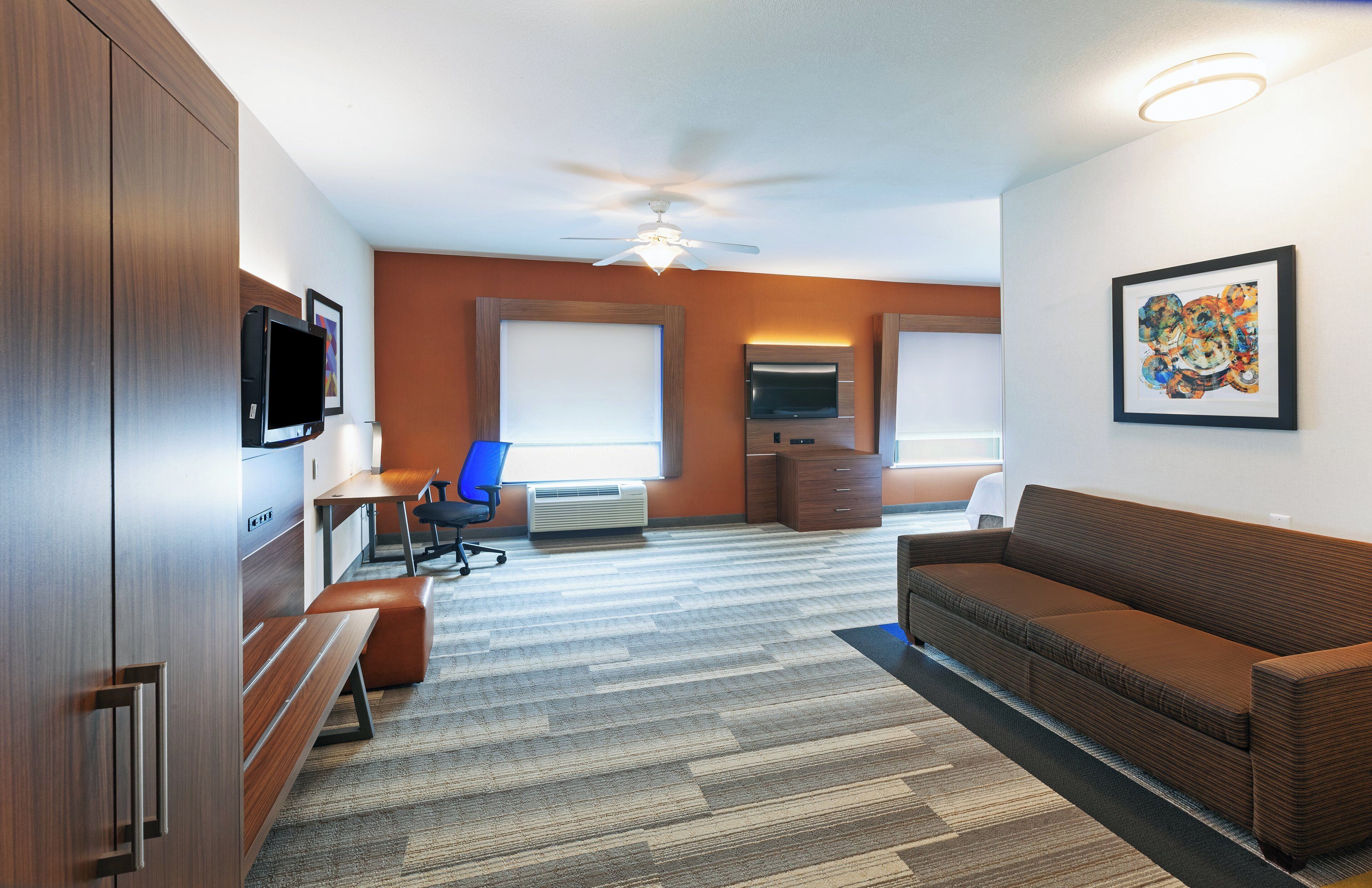 A hotel room with a large bed, a desk with a chair, a sofa, a TV, and a ceiling fan.