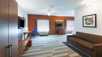 A hotel room with a large bed, a desk with a chair, a sofa, a TV, and a ceiling fan.
