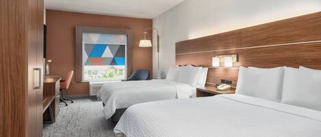 Une chambre d’hôtel avec deux lits, un bureau, une chaise, une lampe et une fenêtre donnant sur un paysage aux formes géométriques.