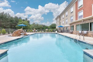 Una piscina con un elemento decorativo de piedra, una zona de estar cubierta y un edificio con ventanas amplias.