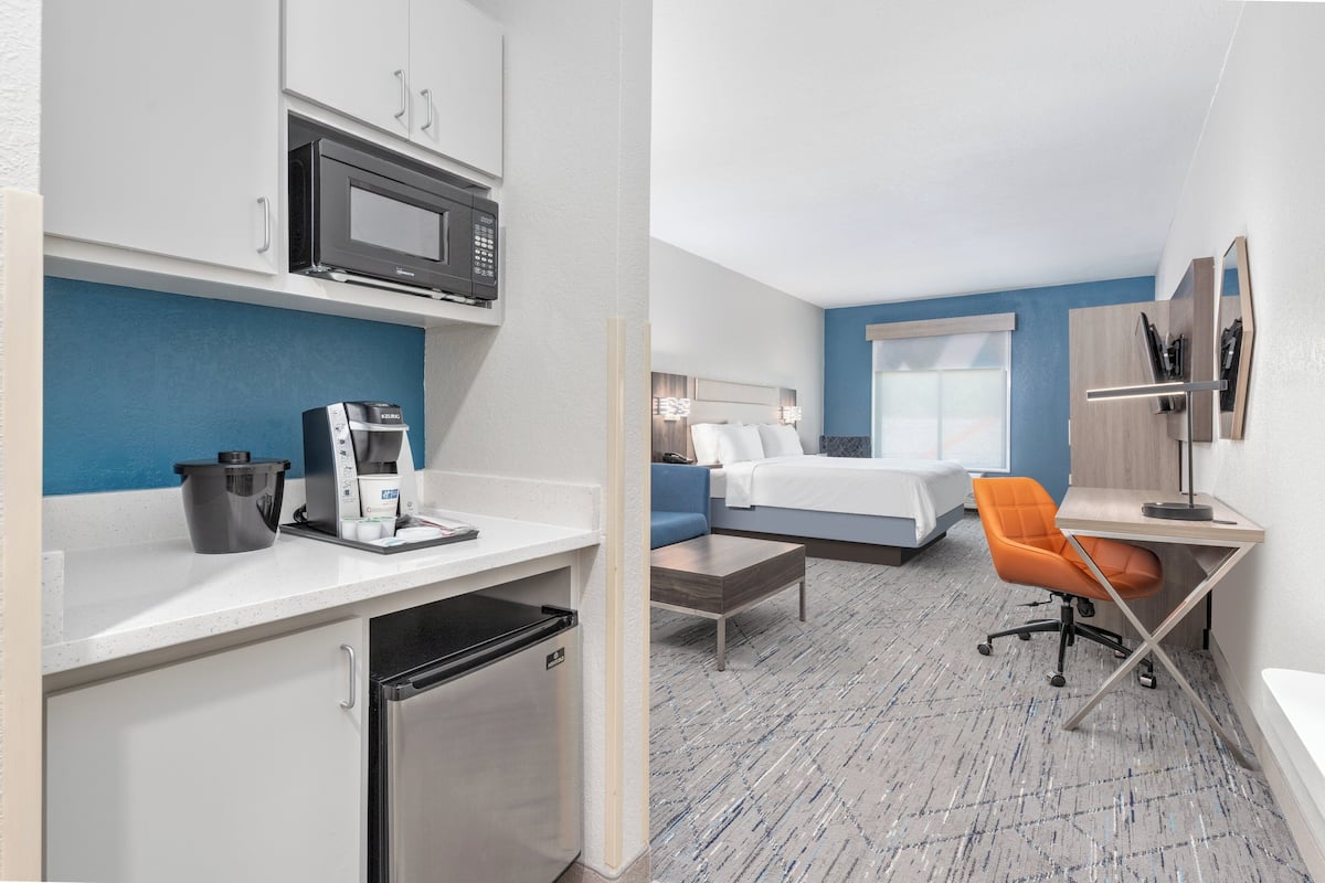 A hotel room with a kitchenette, a bed, a desk, and a chair.