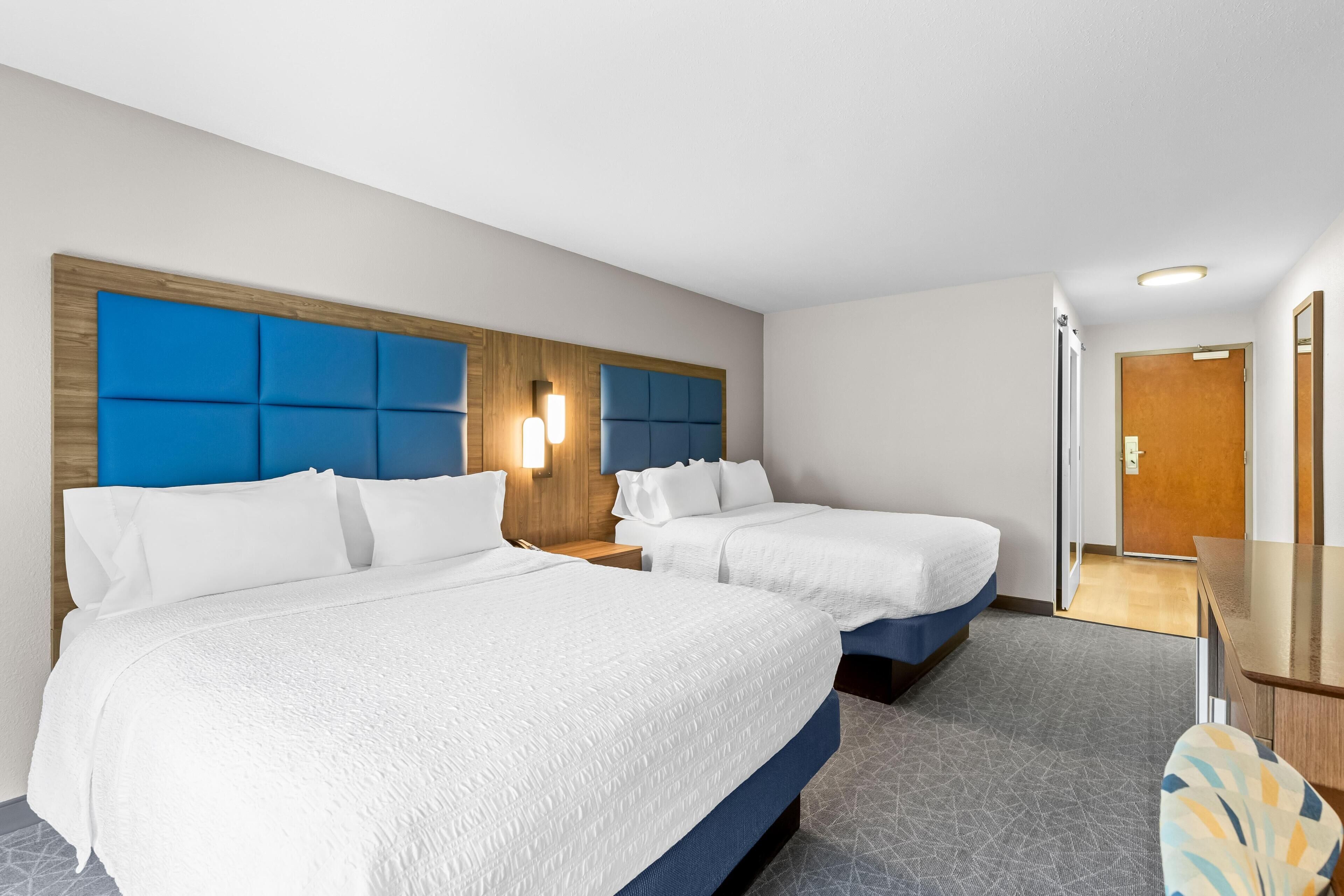 A hotel room with two beds, a wooden headboard, a nightstand, a desk, and a mirror.