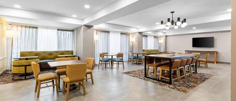 A modern dining area with multiple seating options, including a long table and booths, and a television mounted on the wall.