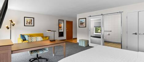 Habitación de hotel con cama, escritorio, silla, sofá, televisor y armario.