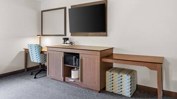 A hotel room with a desk, chair, and a microwave.