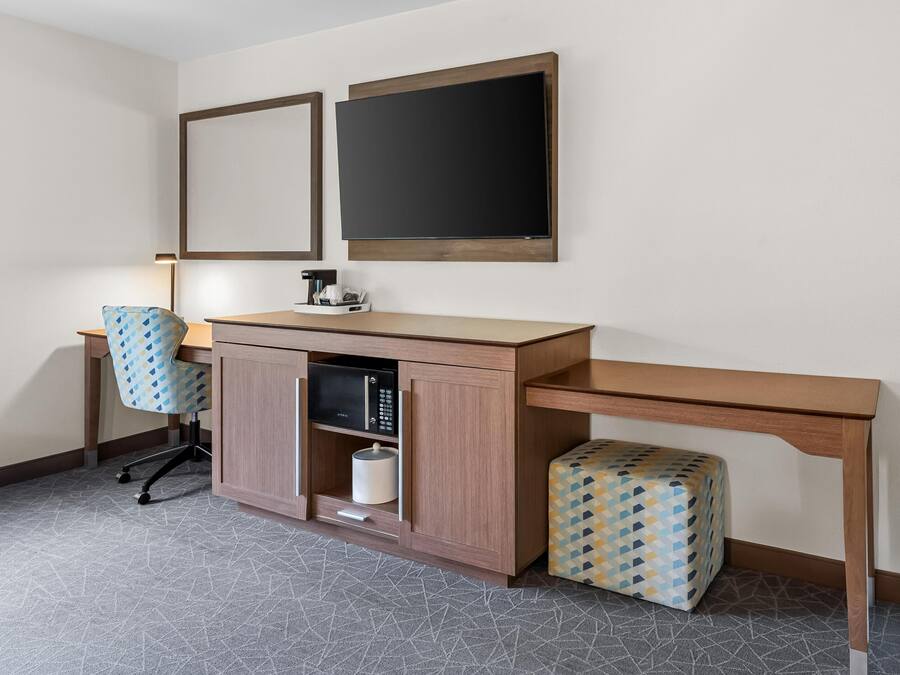 A hotel room with a desk, chair, and a microwave.