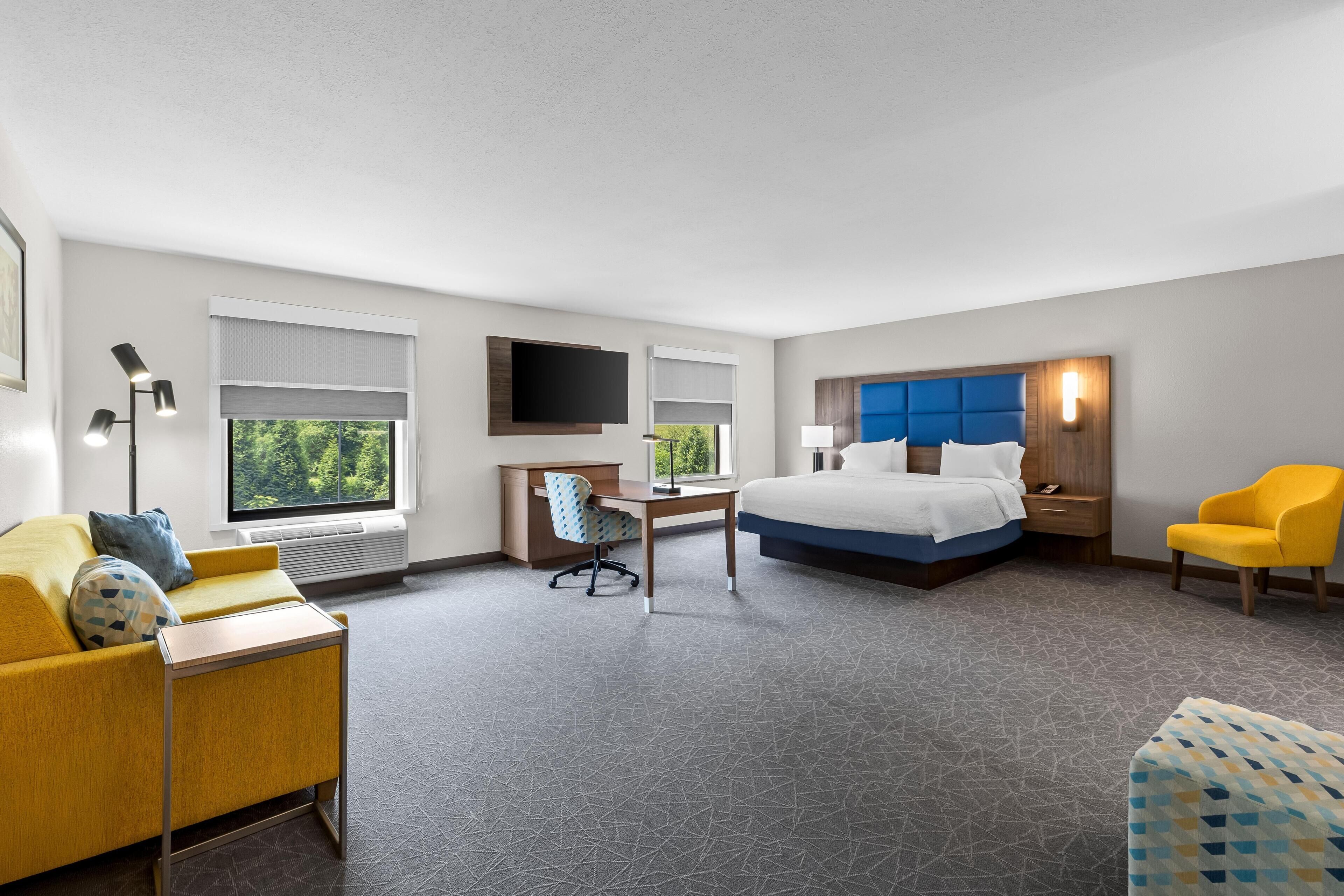 Quarto de hotel com cama, escrivaninha, cadeira e sofá.