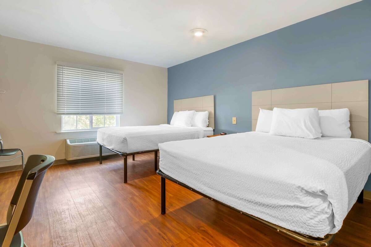 A hotel room with two beds, a desk, and a chair.