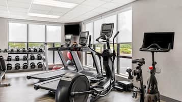 A gym with treadmills, elliptical machines, and a stationary bike. There are dumbbells on racks and a TV mounted on the wall.