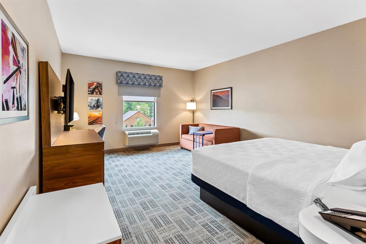 Une chambre d’hôtel avec un lit, un bureau, une chaise, une petite table et une fenêtre donnant sur un bâtiment à l’extérieur.