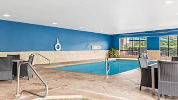 A swimming pool area with a blue wall, a pool ladder, and wicker furniture.
