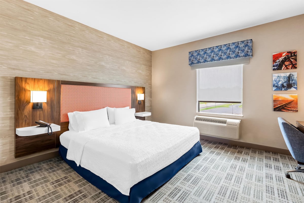 Une chambre d’hôtel avec un grand lit, deux tables de chevet avec des lampes, une fenêtre donnant sur un beau paysage et un climatiseur fixé au mur.