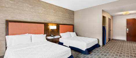 A hotel room with two beds, a small bathroom, and a wooden accent wall.