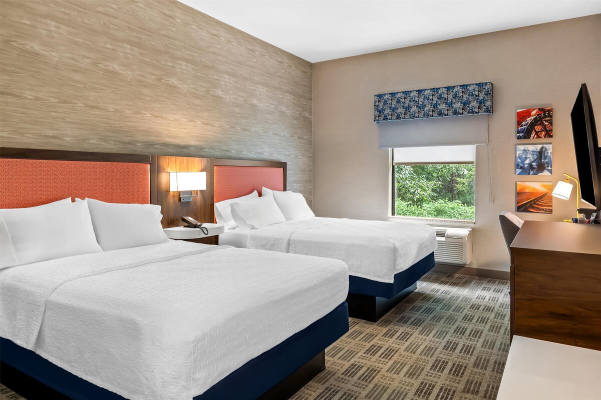 Une chambre d’hôtel avec deux lits, un bureau, une télévision et une fenêtre donnant sur un espace verdoyant.