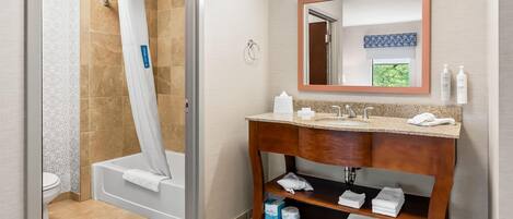 A bathroom with a shower, toilet, vanity, and a mirror.