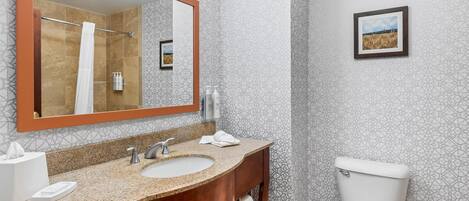 A bathroom with a large mirror, two sinks, a toilet, and a shower.