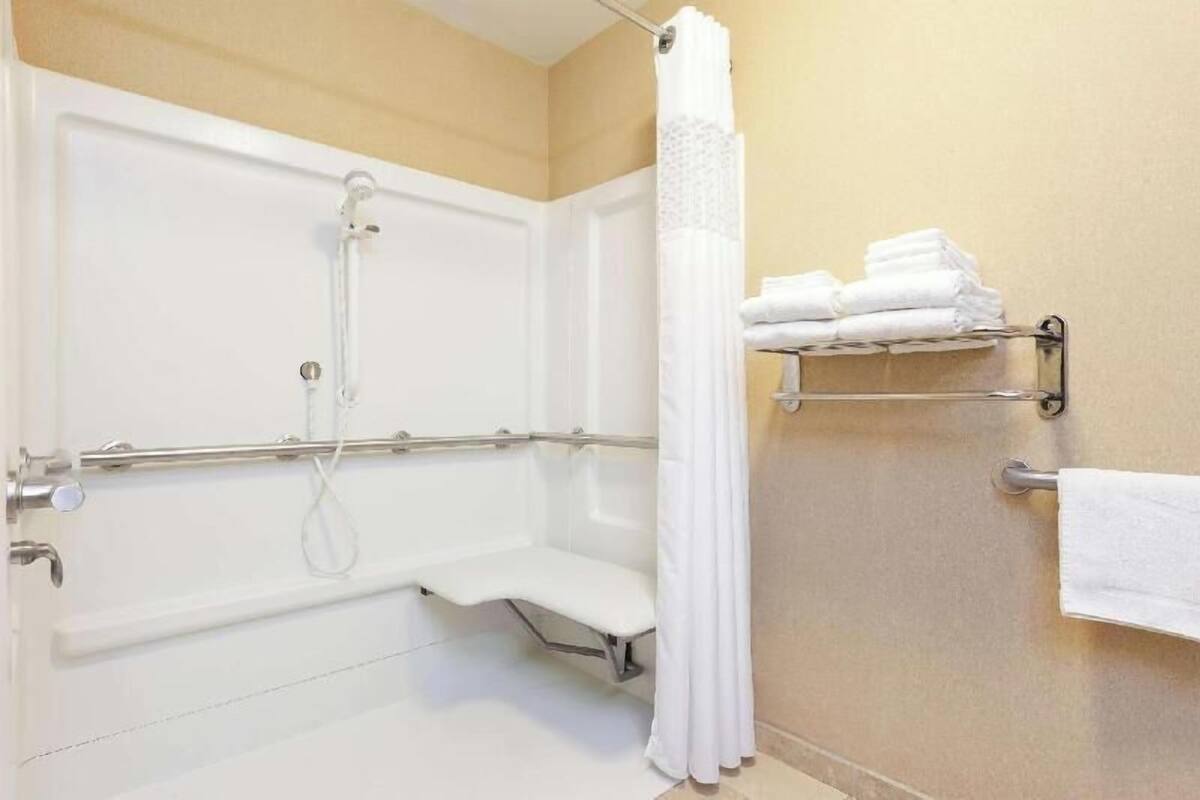 Une salle de bain équipée d’une douche à l’italienne, de barres d’appui, d’un banc, d’un porte-serviettes et d’un rideau de douche.