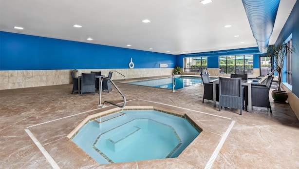 An indoor swimming pool area with a hot tub, seating area, and a view of the outdoors.