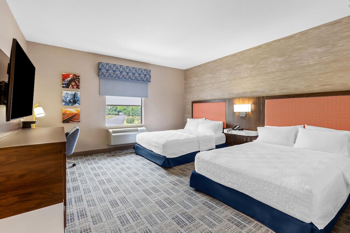 Une chambre d’hôtel avec deux lits, un bureau, une chaise, une télévision et une fenêtre donnant sur un beau paysage.