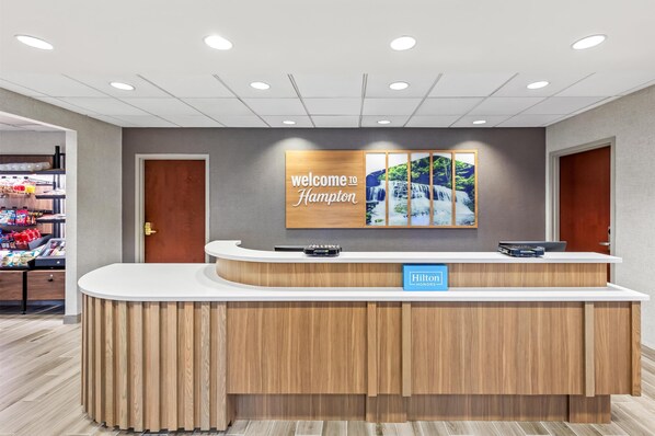 A hotel reception desk with a "Welcome to Hampton" sign and a "Hilton Honors" badge.
