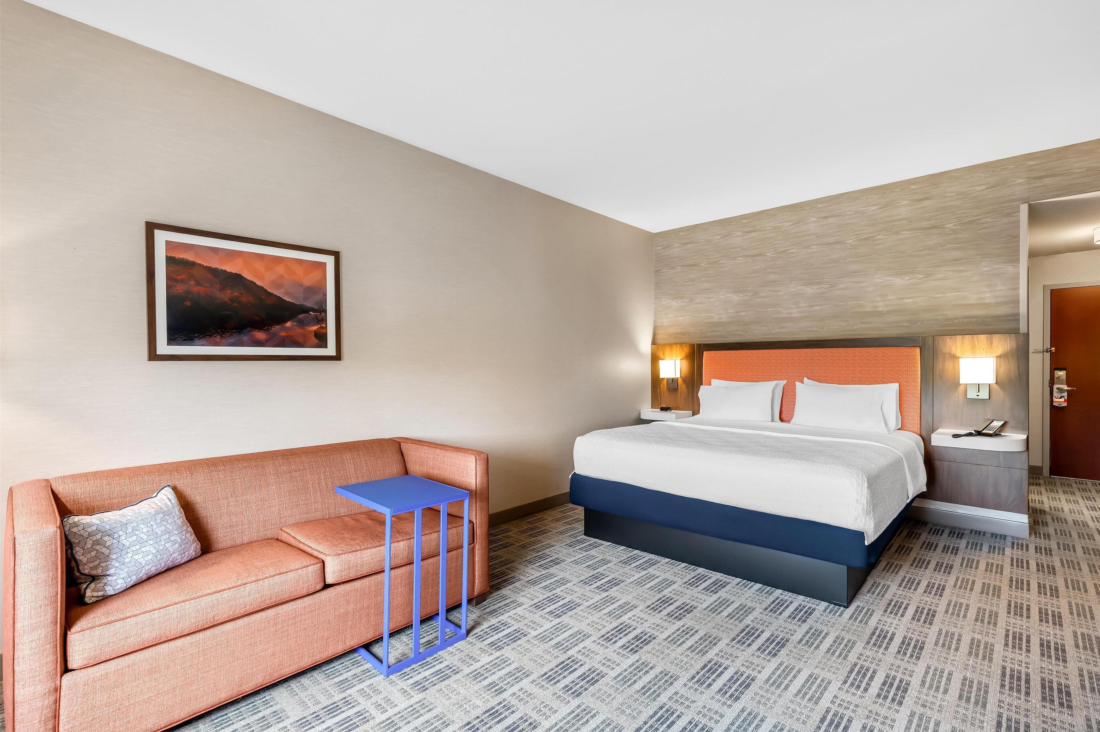 A hotel room with a bed, a sofa, a small table, and a painting on the wall.