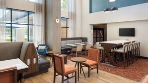 A modern hotel lobby with a seating area, tables, and a TV mounted on the wall. - Hampton Inn & Suites Yuba City (Yuba City)