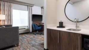 A hotel room with a sofa, a desk, a round mirror, a sink, and a window with curtains. - Hampton Inn & Suites Yuba City (Yuba City)