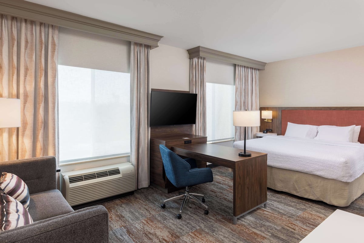Habitación de hotel con cama, escritorio, silla, televisor y ventana con cortinas.
