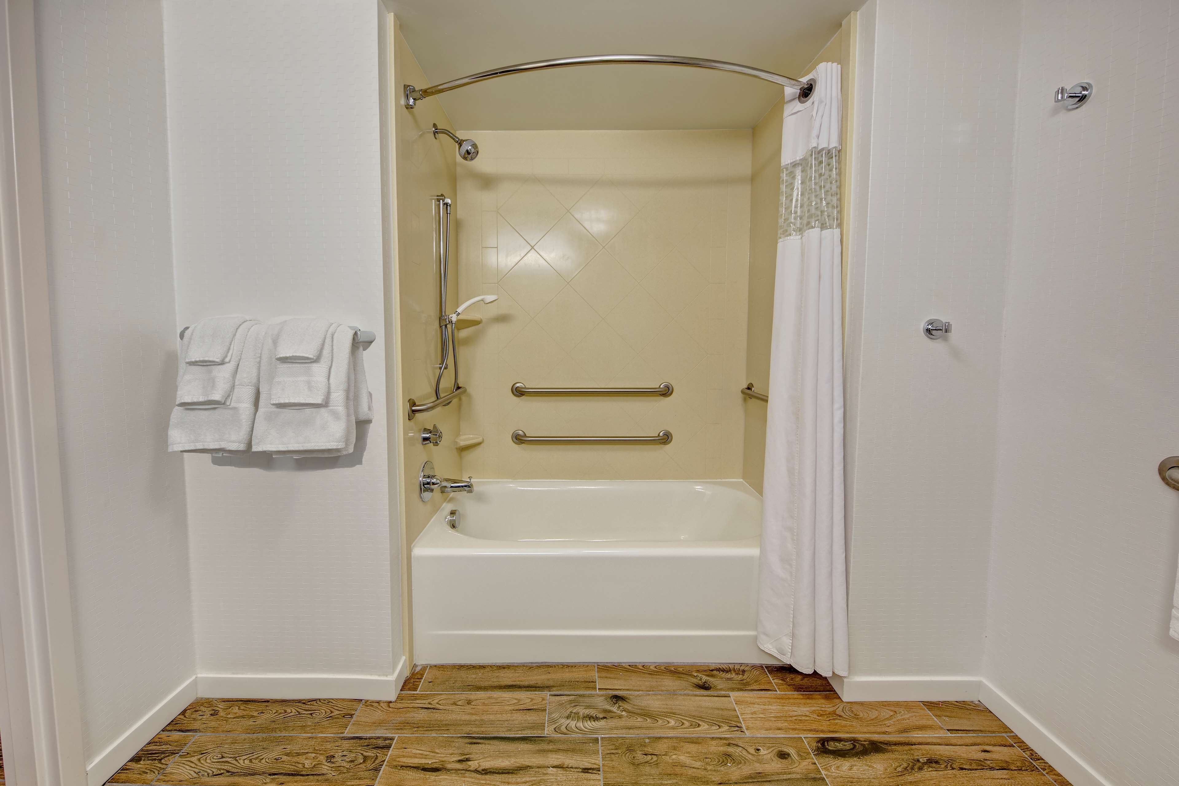A small, white bathroom with a bathtub, a shower, and a toilet. There are two towels hanging on the wall.