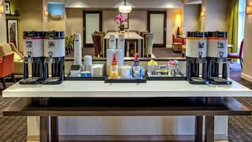 Zona de recepción de un hotel con una estación de café que ofrece varias cafeteras y una variedad de opciones de café y té.